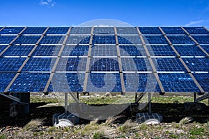 Commercial utility installation of blue photovoltaic panels on a sunny day, foundation pillars below and blue sky above, green pow