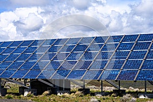 Commercial utility installation of blue photovoltaic panels on a sunny day, foundation pillars below and blue sky above, green pow