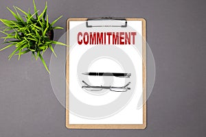 COMMITMENT on the brown clipboard on the grey background. Business concept