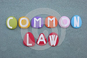 Common law, creative text composed with hand painted multi colored stone letters over green sand