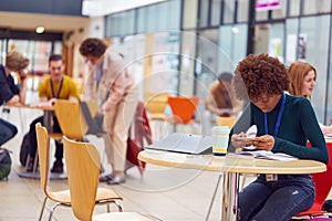 Communal Area Of Busy College Campus With  Female Student Working At Tables And Using Mobile Phone