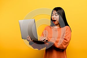 communication concept asian girl use laptop at home yellow studio photo She is happy to spend her free time online while