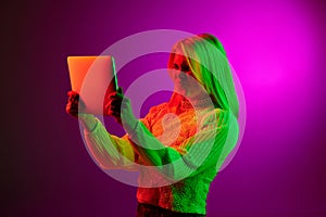 Communication. Emotive young woman having online video call on tablet over magenta studio background in green neon light