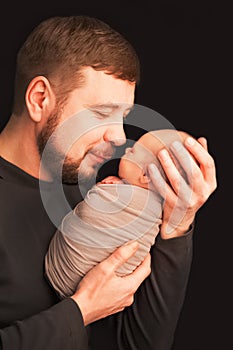 Communication father and son. Holiday concept Father`s Day. Father with a beard holds a newborn in his arms on a black background