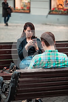 Communication problem man with woman sitting on bench at city street drinking coffee in paper cup looking ito phones