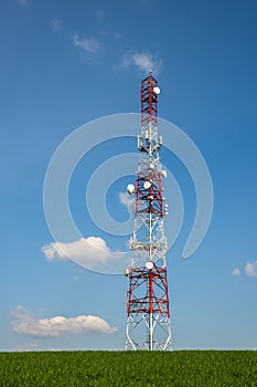 Communication tower on green field against sky