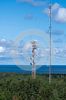 Communication towers rise above pine forests and the sea in the distance