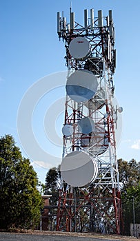 Communications radio tower with satellite dish mobile cell phone against blue sky
