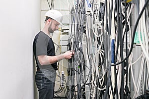 Communications worker is in the arms of a multitude of telecommunication cables. An engineer in a white helmet stands near