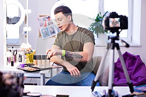 Communicative interested man having different makeup products on the table