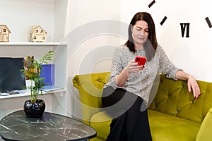 Communicative and responsible girl conducts business correspondence over the phone, at ease on a stylish sofa in a