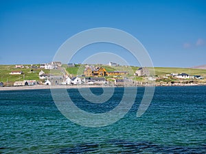 The community of Hillswick in Northmavine, Shetland, UK. Viewed across clear blue water from the Ness of Hillswick on a sunny day