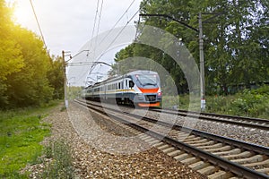 commuter train rides on railway tracks in city with green trees in background