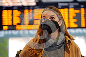 Commuter woman wearing KN95 FFP2 face mask at the airport to protect from virus. Young caucasian woman with timetables information