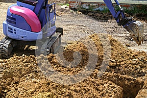 Compact bucket excavator digs clay ground at construction site