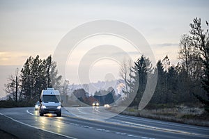 Compact cargo mini van running on turning wet road in twilight with turned on headlight