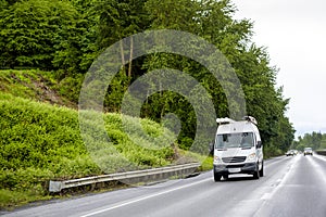 Compact cargo mini van with tubes on the roof running to side of the service driving on the wet highway road at rainy weather photo