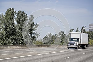 Compact day cab middle power semi truck with box trailer making local deliveries and customer relocation driving on the wide photo