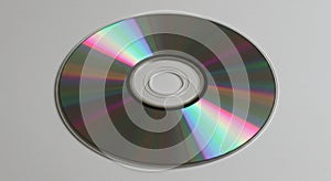 A compact disc (CD) lies on a flat gray surface. The reflective side displays a spectrum