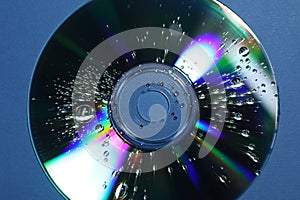 Compact disc with drops on blue background, top view