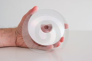 Compact Disc DVD held in hand by Caucasian male hand. Writable side view, close up studio shot,  on white