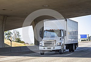 Compact medium power rig semi truck with box trailer running on the highway road under the bridge