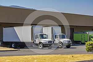 Compact medium size rigs day cab semi trucks with long box trailers for local delivery standing at warehouse dock loading