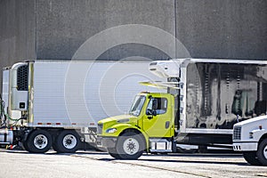 Compact middle duty day cab semi truck with refrigerated box trailer standing in warehouse dock in row with another semi trucks