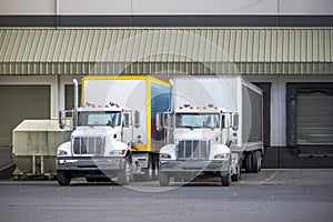 Compact middle duty rigs semi trucks with box trailers standing in warehouse dock loading cargo for next delivery