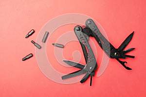 Compact portable black multitool and details on red background, flat lay
