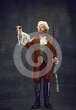 Companion. Portrait of young man in image of nobleman in vintage brown hunting suit and white wig holding cute little