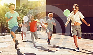Company of active kids are jogning together on the summer city street