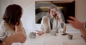 Company employees gathered around a table with coffee mugs, discussing work in a casual setting during a break.