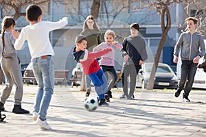 Company of glad children playing football on the street