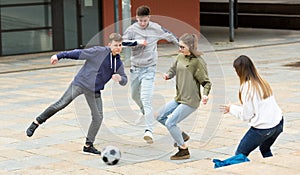 Company of glad teenagers playing football on street