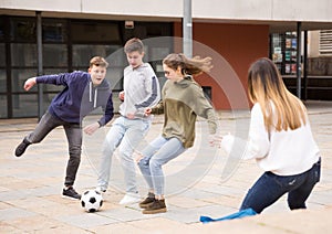 Company of glad teenagers playing football on street