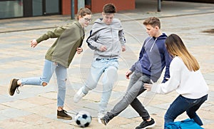 Company of glad teenagers playing football on street