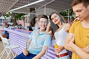 A company of good-looking friends laughing, drinking yellow cocktails and socialising at the bar in the nice summer cafe