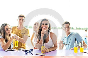 A company of good-looking friends laughing, drinking yellow cocktails and socialising at the bar in the nice summer cafe