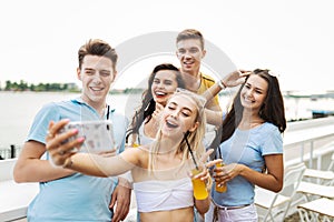 A company of good-looking friends laughing and drinking yellow cocktails and socialising and making selfie in the nice
