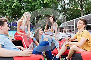 A company of good-looking friends laughing, drinking yellow cocktails and socialising while sitting on the bench and on