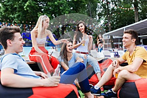 A company of good-looking friends laughing, drinking yellow cocktails and socialising while sitting on the bench and on