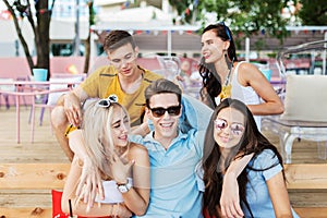 A company of good-looking friends wearing sunglasses laughing and drinking yellow cocktails and socialising at the table
