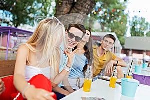 A company of good-looking friends wearing sunglasses laughing and drinking yellow cocktails and socialising at the table