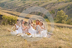 The company of gorgeous female friends having fun, drink wine, and enjoy hills landscape picnic