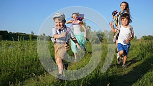Company of happy children with toy windmill laugh and run through meadow