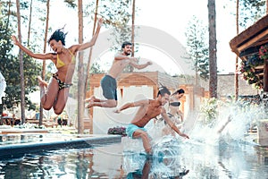 Company of happy young people jumping in pools forming splashes. Swimming pool party concept.