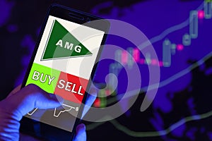 Company logo AFFILIATED MANAGERS GROUP on smartphone screen, hand of trader holding mobile phone showing BUY or SELL on background