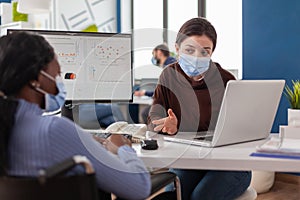 Company manager with mask explaining to paralysed african colleague project plan