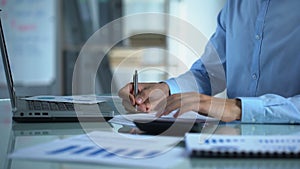 Company marketer counting calculator and filling report, sitting at office table